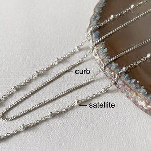 May include: Two silver chains, one curb chain and one satellite chain, are laid out on a brown stone surface. The chains are labeled "curb" and "satellite".