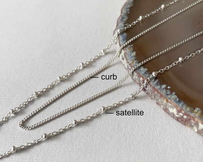 May include: Two silver chains, one curb chain and one satellite chain, are laid out on a brown stone surface. The chains are labeled "curb" and "satellite".