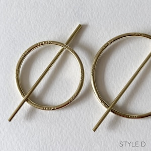 May include: A pair of gold-toned earrings with a circle design and a bar that goes through the circle. The earrings are marked with "STYLE D".