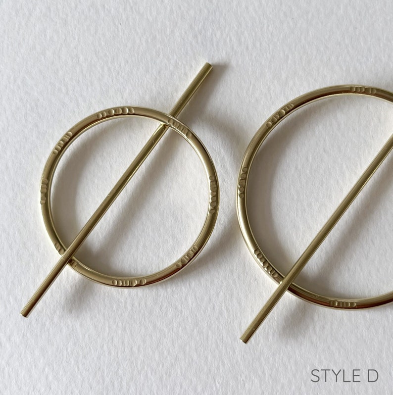 May include: A pair of gold-toned earrings with a circle design and a bar that goes through the circle. The earrings are marked with "STYLE D".