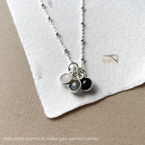 May include: A silver chain necklace with three charms: a white stone, a gray stone, and a black stone.