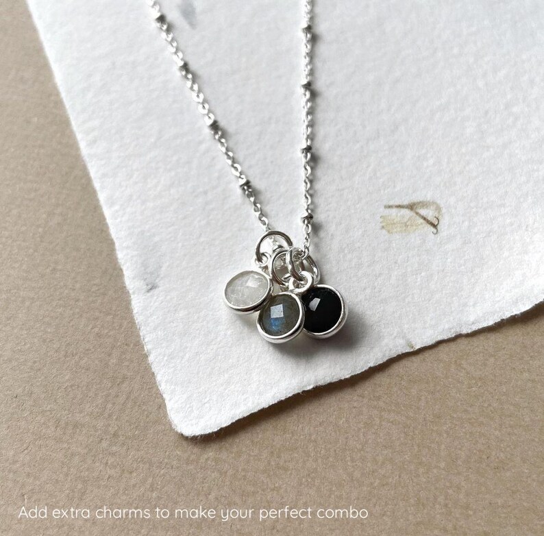 May include: A silver chain necklace with three charms: a white stone, a gray stone, and a black stone.