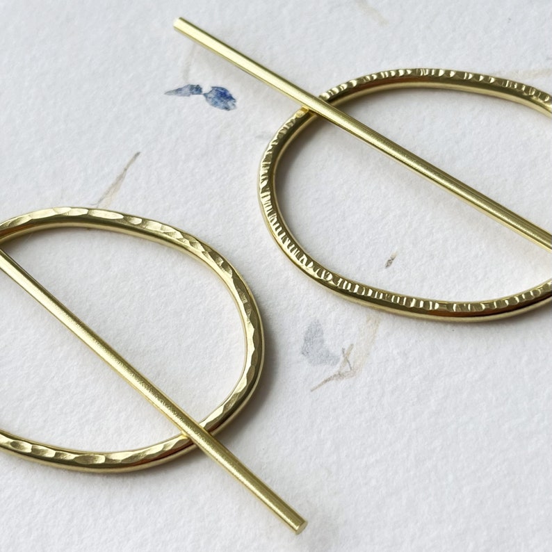 May include: A pair of gold-toned earrings with a hammered oval shape and a straight bar that goes through the center of the oval.