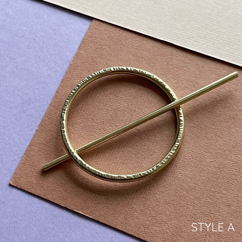 May include: A gold-toned metal hair clip with a textured circular design and a straight bar that goes through the circle. The text "STYLE A" is visible in the bottom right corner of the image.
