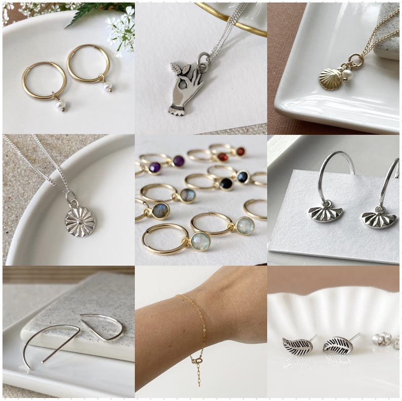 May include: A collection of silver and gold jewelry featuring various designs, including a hand holding a heart, a seashell, a flower, a leaf, and a crescent moon. The jewelry is displayed on a white background.