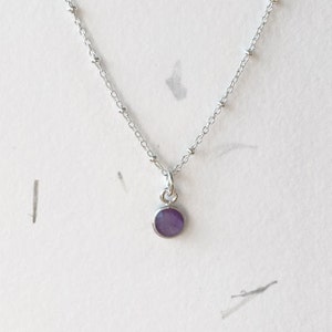 May include: A silver chain necklace with a small round purple gemstone pendant.