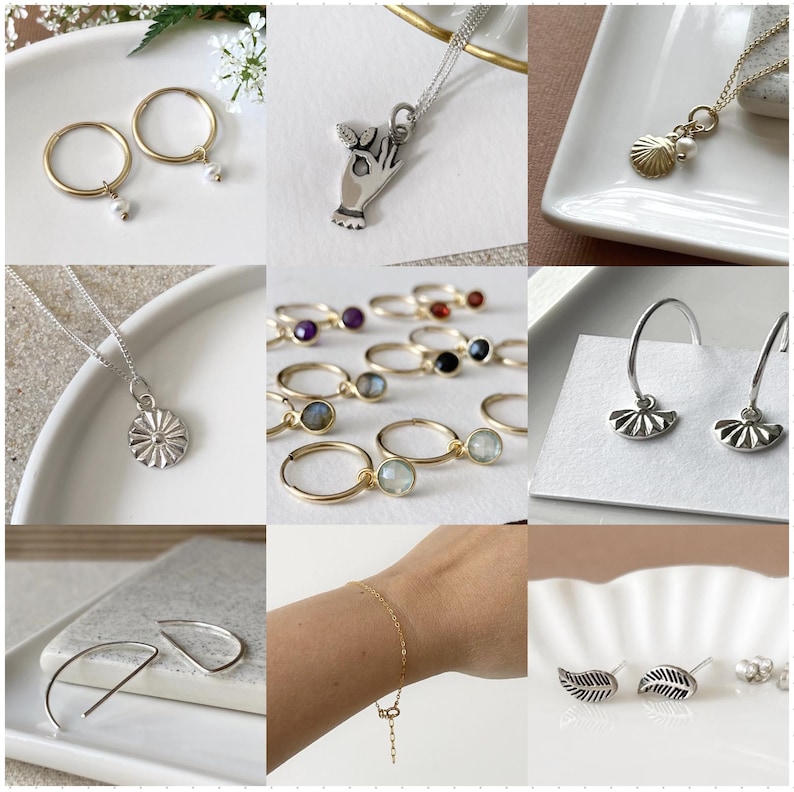 May include: A collection of silver and gold jewelry featuring various designs, including a hand holding a heart, a seashell, a flower, a leaf, and a crescent moon. The jewelry is displayed on a white background.