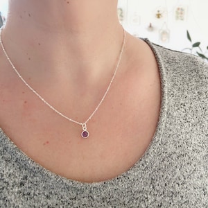 May include: A silver chain necklace with a small, round, purple gemstone pendant.