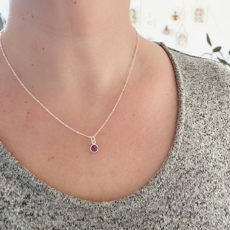 May include: A silver chain necklace with a small, round, purple gemstone pendant.