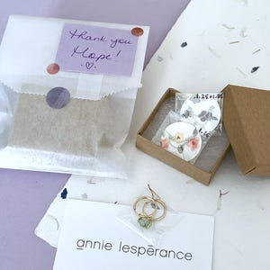 May include: A small, brown cardboard box with a white card inside. The card has a floral design and the text "1.25 + 1.45". The box is sitting on a white surface with a handwritten note that says "Thank you Hope!" and a heart.