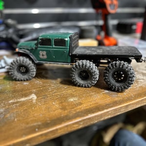 Peut inclure: Un camion jouet vert avec une benne et quatre grandes roues noires. Le camion a une cabine noire avec des fen&ecirc;tres et un pare-chocs noir. Le camion est pos&eacute; sur une surface en bois.