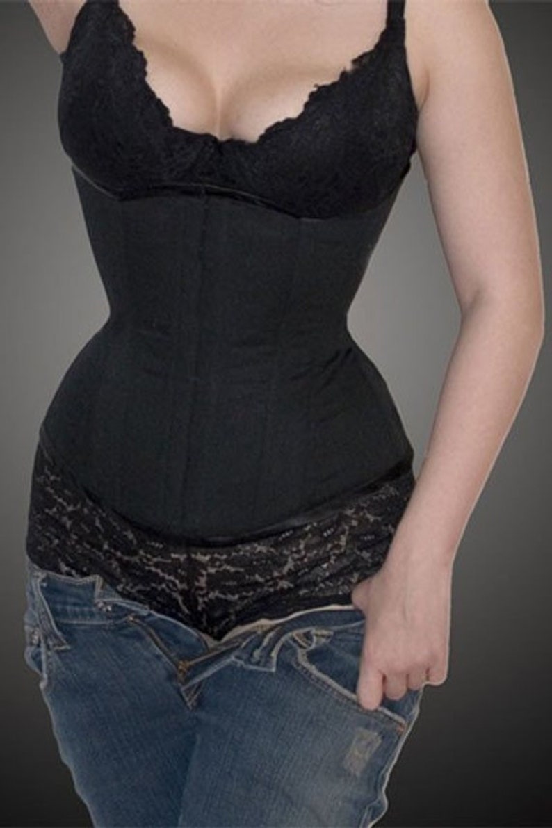 Pode incluir: Um espartilho preto com acabamento em renda e um top de renda preto a condizer. O espartilho &eacute; usado com jeans azuis. A imagem &eacute; um plano m&eacute;dio, com foco no torso e na cintura.