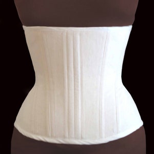 May include: A white cotton corset with a smooth, flat front and a series of vertical seams. The corset is designed to cinch the waist and create a more defined silhouette.