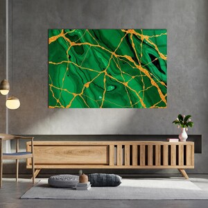 Könnte beinhalten: Ein großes rechteckiges Wandkunstwerk mit einem grünen Marmormuster und goldenen Adern. Das Kunstwerk ist an einer grauen Wand über einem Holzschrank angebracht. Der Raum hat eine moderne, minimalistische Ästhetik.