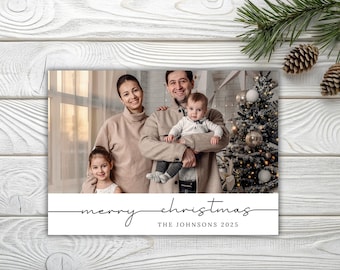 Op de afbeelding: Een kerstkaart met een familiefoto en een versierde kerstboom. De kaart leest "merry christmas" en "THE JOHNSONS 2025" in een scriptlettertype. De afbeelding staat tegen een houten achtergrond.