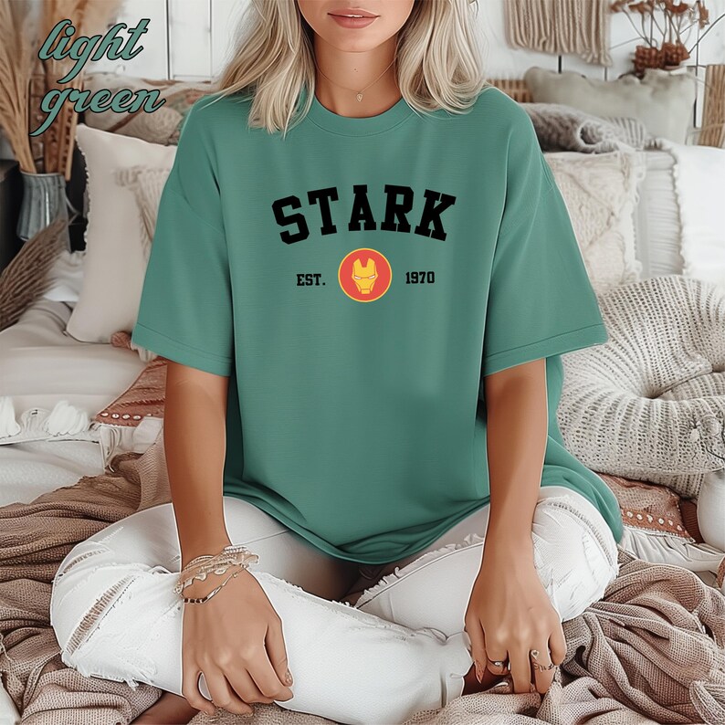 May include: A light green t-shirt with the text "STARK EST. 1970" and a red and gold logo.