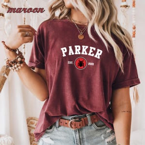 May include: A maroon t-shirt with white text that reads "Parker Est. 2001" and a red circle with a black spider inside.