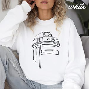 Pu&ograve; includere: Felpa bianca con un disegno a linea nera di R2-D2 di Star Wars.