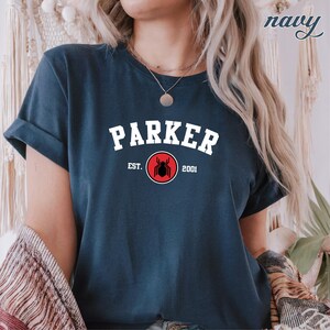 May include: A navy blue t-shirt with white text that reads "Parker Est. 2001" and a red circle with a black spider graphic.