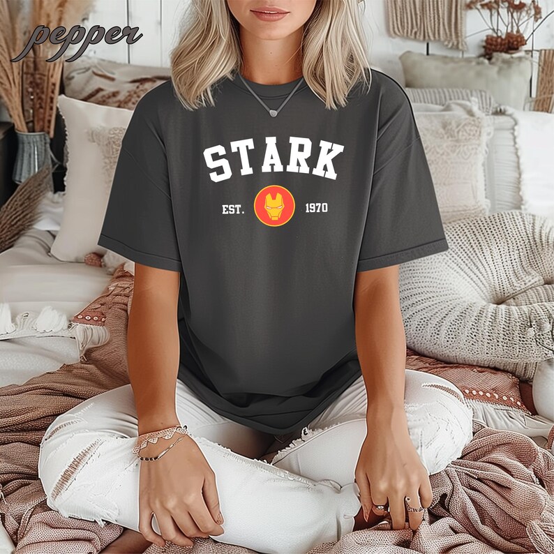 May include: A dark gray t-shirt with the text "STARK EST. 1970" and a red and yellow iron man logo.
