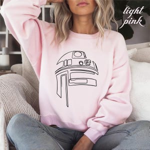 Pu&ograve; includere: Una felpa rosa chiaro con un disegno a linea nera di R2-D2 di Star Wars.