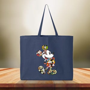 May include: Navy blue tote bag with a colourful Mickey Mouse design. The cartoon character is made up of various images of Mickey Mouse. The bag has two handles and is made of a sturdy fabric. The background is a blurred wooden surface.
