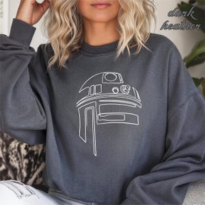 Pu&ograve; includere: Una felpa grigia melange scuro con un contorno bianco di R2-D2 di Star Wars.