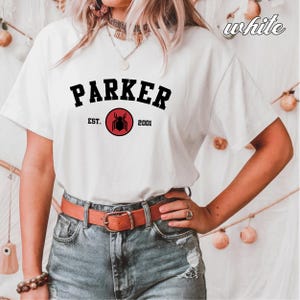 May include: White t-shirt with black text that reads "PARKER EST. 2001" and a red circle with a black spider graphic.