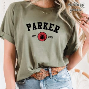 May include: A green t-shirt with the text "PARKER" in black letters in an arch above a red circle with a black spider inside. The text "EST. 2001" is below the circle.