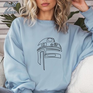 Pu&ograve; includere: Una felpa di colore azzurro chiaro con un disegno a linea nera di R2-D2 di Star Wars.