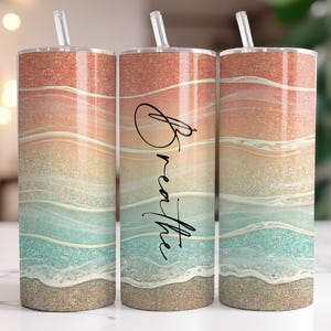 Pode incluir: Um conjunto de três canecas de aço inoxidável com um design de praia. As canecas apresentam um gradiente de cores, incluindo coral, areia e turquesa, com a palavra "Breathe" em itálico. Cada caneca tem uma palhinha transparente.