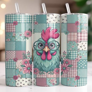 May include: Three stainless steel tumblers with straws. Each tumbler has a patchwork design in teal, pink, and white, with floral and gingham patterns. The central tumbler shows a cartoon rooster wearing glasses, surrounded by flowers.