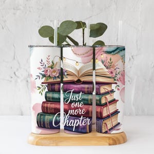 May include: A white tumbler with a floral and book design. The design features a stack of books with an open book on top, fairy lights, and the text "Just one more chapter."