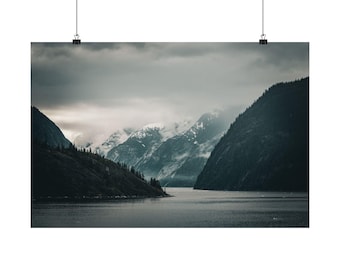 May include: A landscape wall art print featuring a dark, moody fjord scene with steep, shadowed mountains flanking a calm body of water. The peaks are partially obscured by low-hanging clouds and mist, creating a somber, atmospheric view.