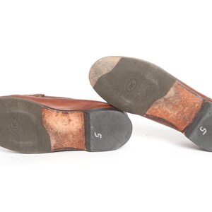 May include: A pair of brown leather loafers with a brown leather sole. The loafers have a size 5 printed on the sole.
