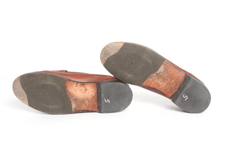 May include: A pair of brown leather loafers with a brown leather sole. The loafers have a size 5 printed on the sole.
