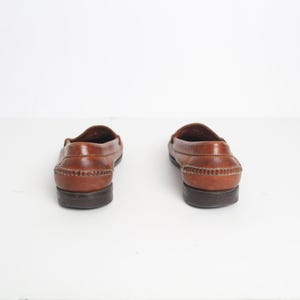 May include: A pair of brown leather loafers with a stitched detail around the edge of the sole.