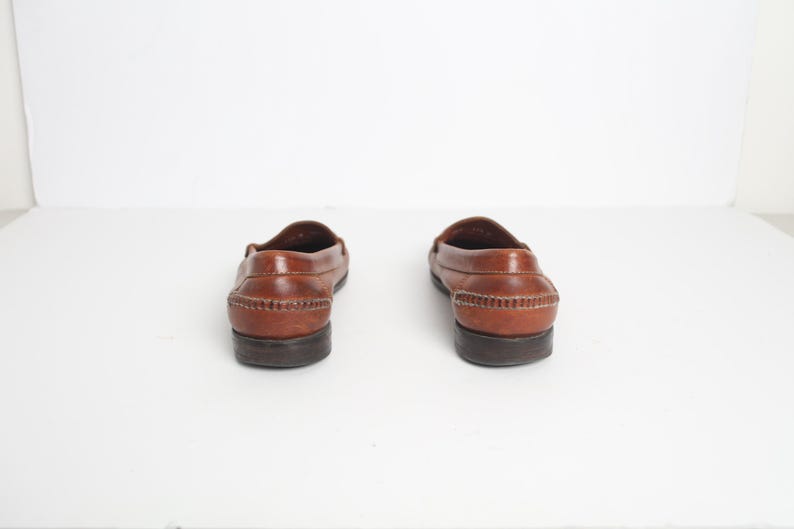 May include: A pair of brown leather loafers with a stitched detail around the edge of the sole.
