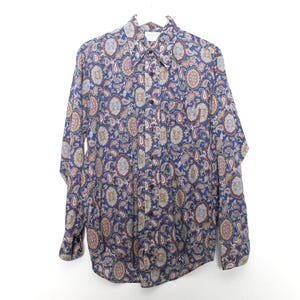 May include: A long-sleeve button-down shirt featuring a dense, intricate paisley pattern in shades of blue, gold, and cream. The shirt has a pointed collar, a front button placket with dark buttons, and buttoned cuffs on the long sleeves.