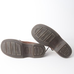 May include: A pair of brown leather lace-up shoes with a textured sole. The shoes have the word "SKECHERS" printed on the sole.
