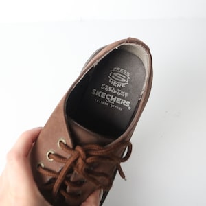 May include: Brown leather lace-up shoes with a brown lace and a white label inside that reads "Press Here Feel the Comfort Skechers USA Leather Uppers."