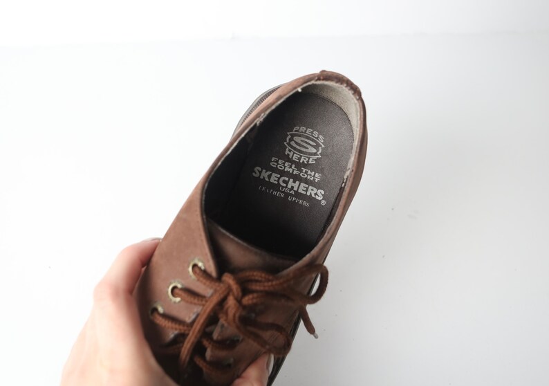 May include: Brown leather lace-up shoes with a brown lace and a white label inside that reads "Press Here Feel the Comfort Skechers USA Leather Uppers."
