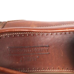 May include: Close-up of the inside of a brown leather shoe. The insole is brown leather with the text "Johnston & Murphy" embossed in the leather.