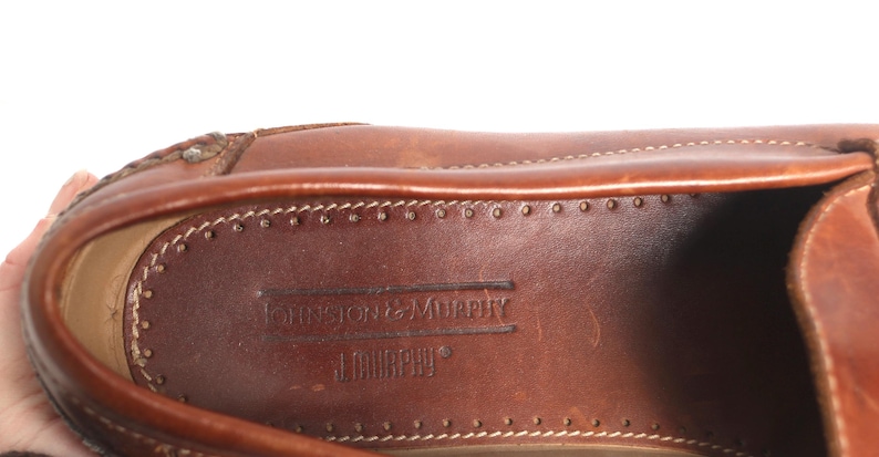 May include: Close-up of the inside of a brown leather shoe. The insole is brown leather with the text "Johnston & Murphy" embossed in the leather.