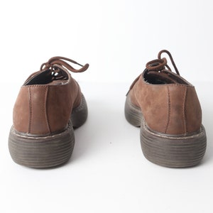 May include: A pair of brown leather lace-up shoes with thick soles. The shoes are worn and have a distressed look.