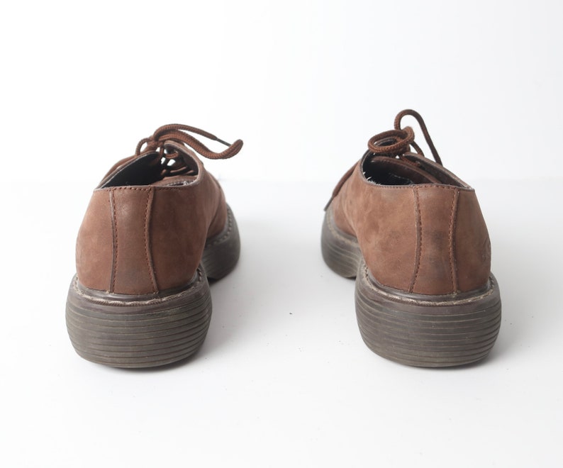 May include: A pair of brown leather lace-up shoes with thick soles. The shoes are worn and have a distressed look.