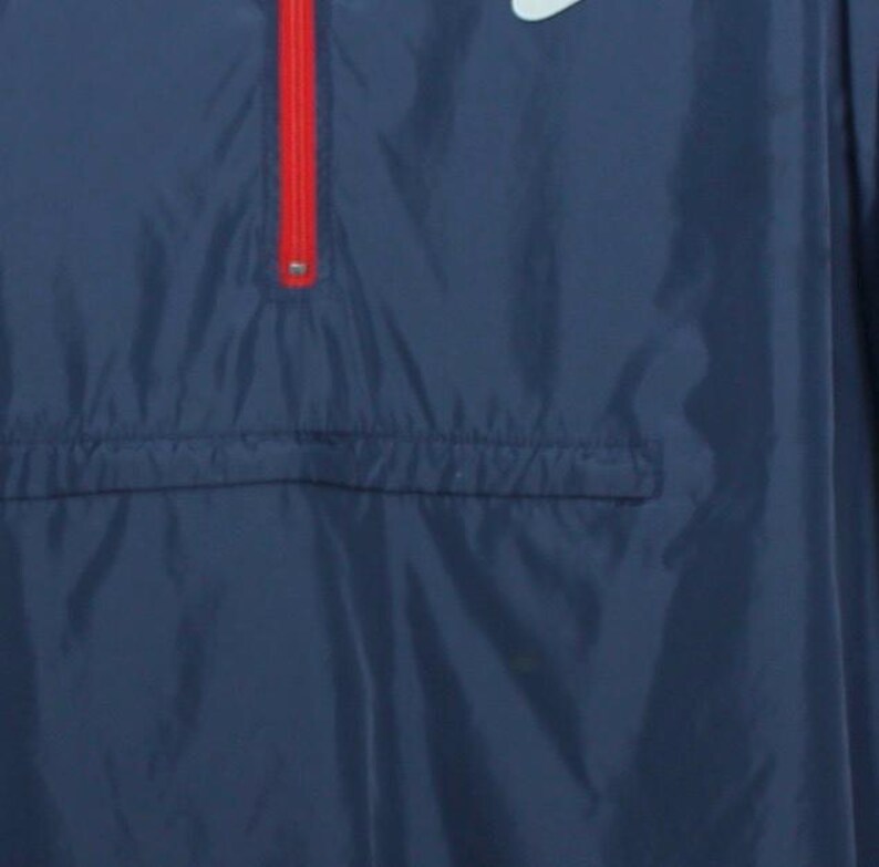 May include: Navy blue windbreaker jacket with a red zipper and a white logo. The jacket has a front pocket and a drawstring at the bottom. The jacket is made of a lightweight material.