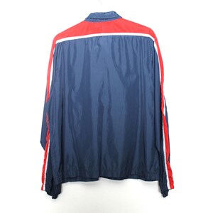 May include: A navy blue jacket with a red upper back panel and red and white stripes down the sleeves. The jacket has a collared neckline and is hanging on a white hanger.