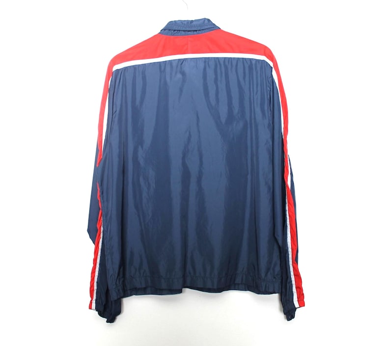 May include: A navy blue jacket with a red upper back panel and red and white stripes down the sleeves. The jacket has a collared neckline and is hanging on a white hanger.