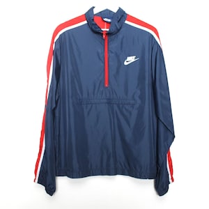 May include: Navy blue Nike windbreaker jacket with red and white stripes on the sleeves. Features a red zipper and the Nike logo in white on the chest. A classic athletic outerwear piece.
